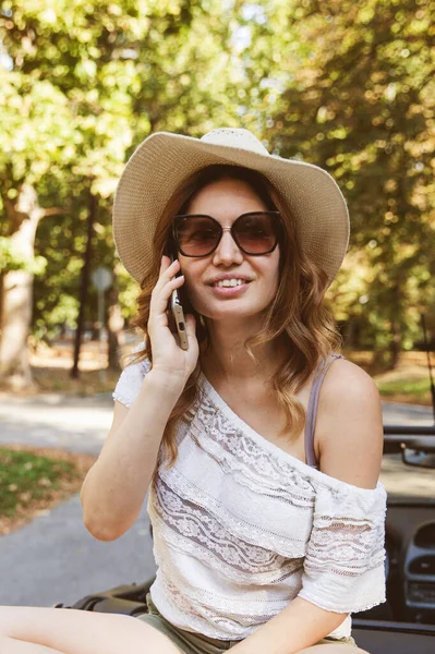 Portrait of beautiful woman speaking by phone in the park. Summer day, natural light