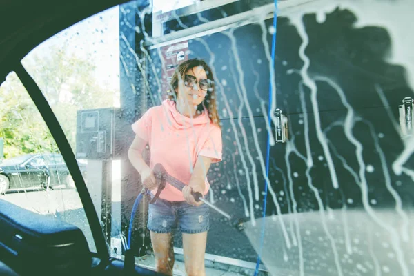 妇女在自助洗车站用高压喷雾器洗车 透过车窗看到 — 图库照片