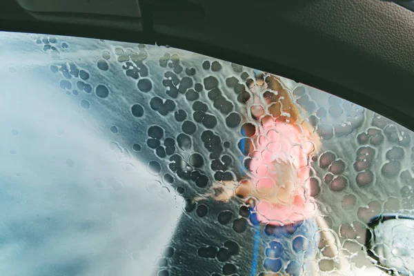 車の窓から見える セルフサービスの車の洗浄ステーションで高圧噴霧器で彼女の車を洗う女性 — ストック写真