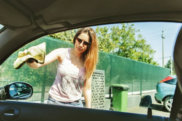 Woman cleaning car window with cloth, seen through car window
