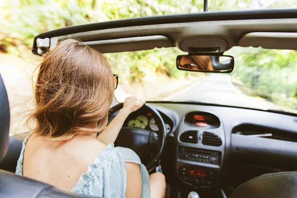 夏の日にコンバーチブル車を運転するかなり若い女性 サングラスをかけて 車のリアビューミラーに反射します 女性ドライバーのバックビュー 肩越しの眺め — ストック写真