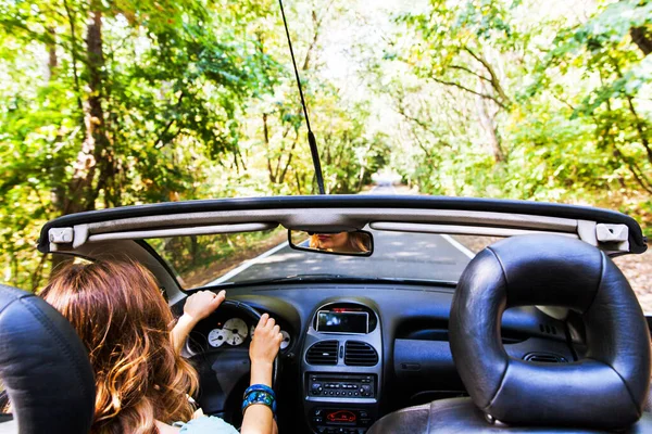 夏の日にコンバーチブル車を運転するかなり若い女性 サングラスをかけて 車のリアビューミラーに反射します 女性ドライバーのバックビュー 肩越しの眺め — ストック写真