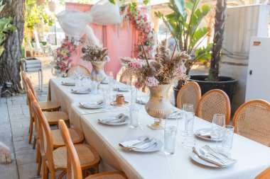 Zarif bir açık hava yemek masası. Çiçekli süslemelerle süslenmiş. Düğün, parti ya da özel bir kutlama için hazır.