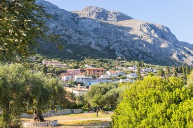 Renkli evler ve zeytin ağaçları, açık mavi gökyüzünün altında yemyeşil ve kayalık dağlarla dolu Akdeniz yamaçlarındaki bir köyü süslüyor..