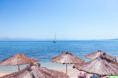 Geleneksel saman şemsiyeleriyle güzel, güneşli çakıl taşı plajları, sakin mavi denizde zarifçe yüzen bir yelkenliyle rahatlamak için mükemmel bir yer sağlar..