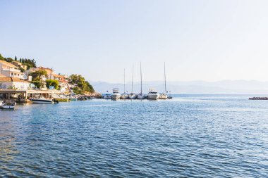 Küçük bir Akdeniz kıyı köyünün panoramik ve huzurlu manzarası. Limanı demirlemiş teknelerle dolu, açık bir günde uzak dağların arka planına kurulmuş..