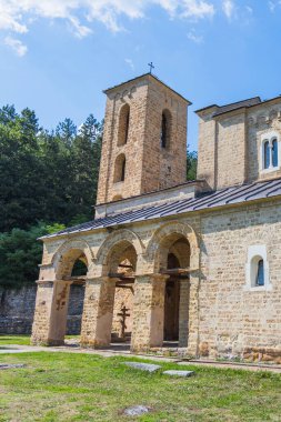 Studenica Manastırı 'nın tarihi taş çan kulesi ve kemerli kapısının detaylı bir görüntüsü, parlak mavi bir gökyüzünün altında, dini, kültürel veya miras hikayeleri için ideal ahşap bir haç yer alıyor..