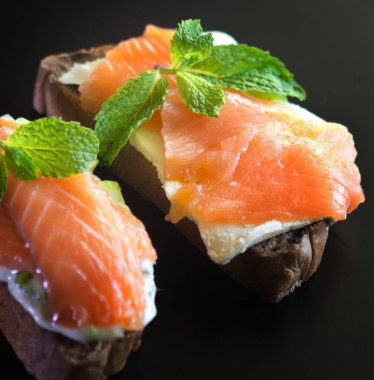 Siyah arka planda kırmızı balıklı iki sandviç.