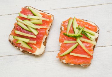 Kırmızı balıklı iki sandviç ve ahşap zemin üzerinde salatalık.