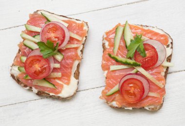 Kırmızı balıklı, domatesli, turplu ve ahşap kaplamalı iki sandviç.