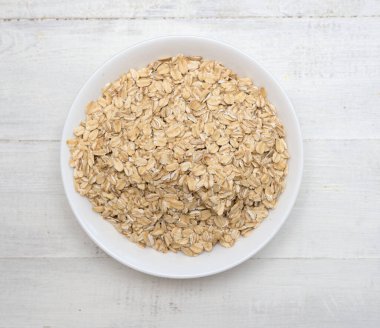 Tahta bir zeminde beyaz tabakta kuru yulaf ezmesi.