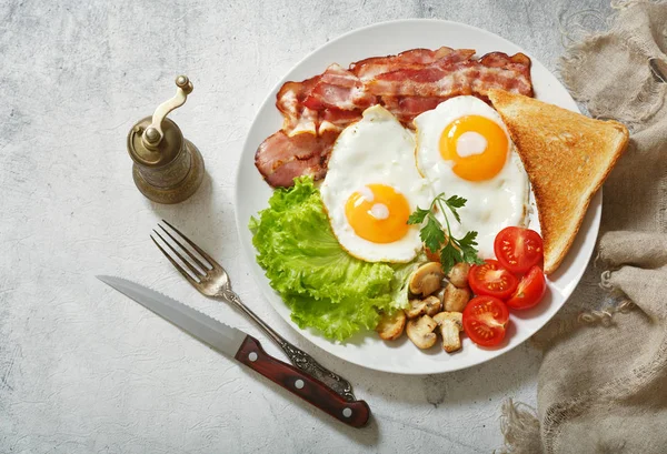 breakfast with plate of fried eggs, bacon, mushrooms and toast, top view