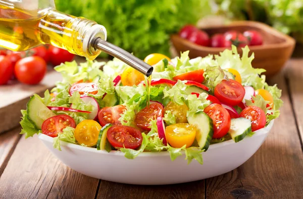 Cooking salad. olive oil pouring into bowl of fresh vegetable salad