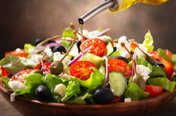 olive oil pouring into bowl of fresh salad with vegetables, feta