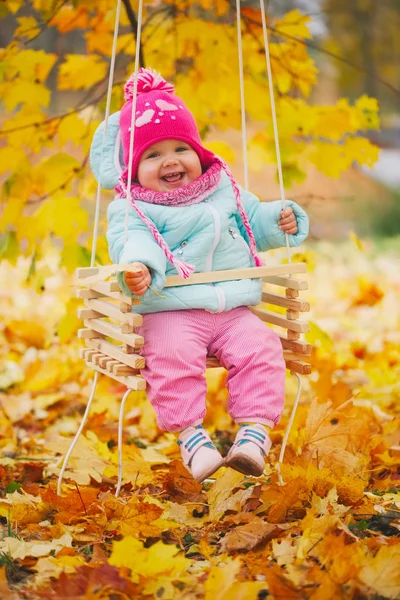 Маленькая девочка на качелях в осеннем парке — стоковое фото
