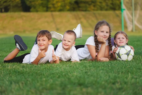 Happy children lying on football pitch — Stock Photo, Image