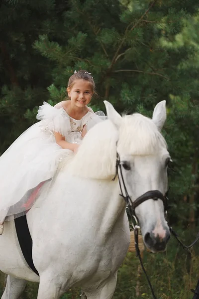 Счастливая маленькая девочка на белом коне в лесу — стоковое фото
