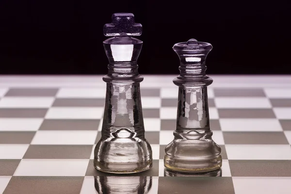黒と白でお互いに直面して王と王妃のガラス チェスの駒 ロイヤリティフリーのストック写真