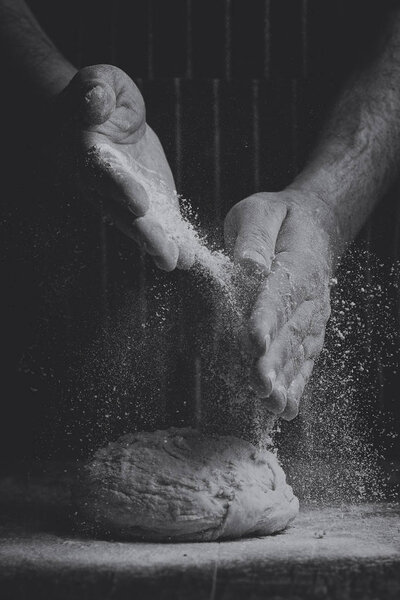 Мука посыпается на шар теста на деревянную доску вручную в художественном преобразовании
