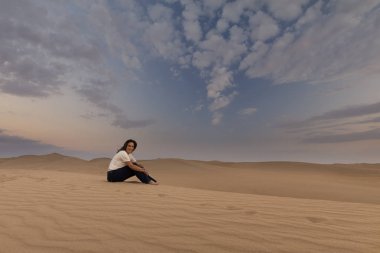 Güneşin tadını bir çölde bir kumul üzerinde oturan kadın