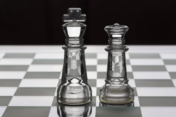 Rey y reina pieza de ajedrez de vidrio uno frente al otro en negro y — Foto de Stock