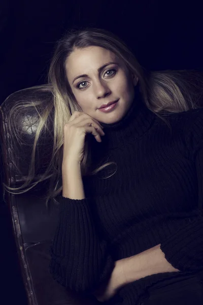 Beautiful woman in low light sitting on a leather sofa artistic — Stock Photo, Image