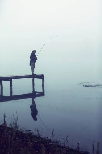 Uomo con attrezzi da pesca a mosca cattura di una trota dal molo su una nebbia — Foto Stock