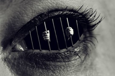 Bir hapishanenin parmaklıklarını insan gözünün içinde tutan ellerin kavramsal monokrom fotoğrafı
