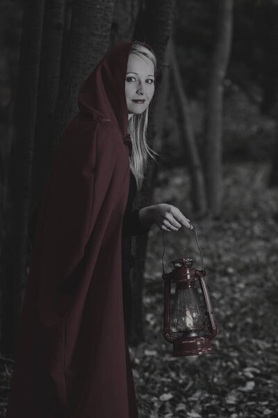 Attractive woman dressed a little red riding-hood walk in a dark forest with a lantern