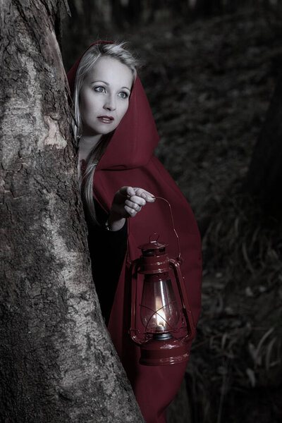 Attractive woman dressed a little red riding-hood walk in a dark forest with a lantern