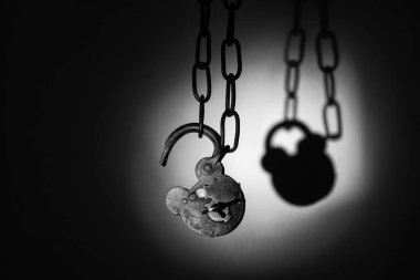 Eski, yıpranmış asma kilit bir zincir üzerinde kırılır, paslı şekli lekeli bir duvara karşı koyu bir gölge bırakır..