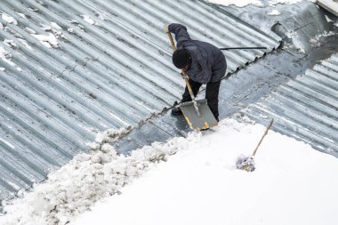 Bir adam kaldırır kar küreği üstten görünüm, metal çatı.