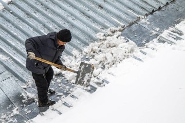 Bir adam kaldırır kar küreği üstten görünüm, metal çatı.