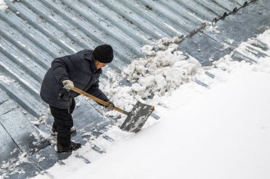 Bir adam kaldırır kar küreği üstten görünüm, metal çatı.