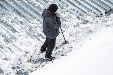 Bir adam kaldırır kar küreği üstten görünüm, metal çatı.