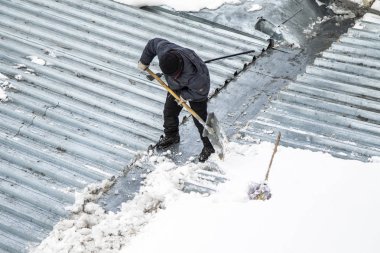 Bir adam kaldırır kar küreği üstten görünüm, metal çatı.
