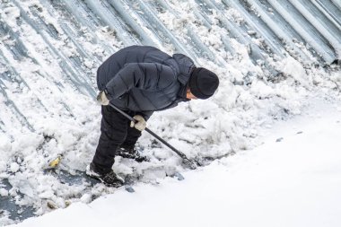 Bir adam kaldırır kar küreği üstten görünüm, metal çatı.