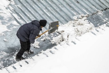 Bir adam kaldırır kar küreği üstten görünüm, metal çatı.