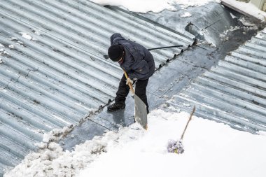 Bir adam kaldırır kar küreği üstten görünüm, metal çatı.