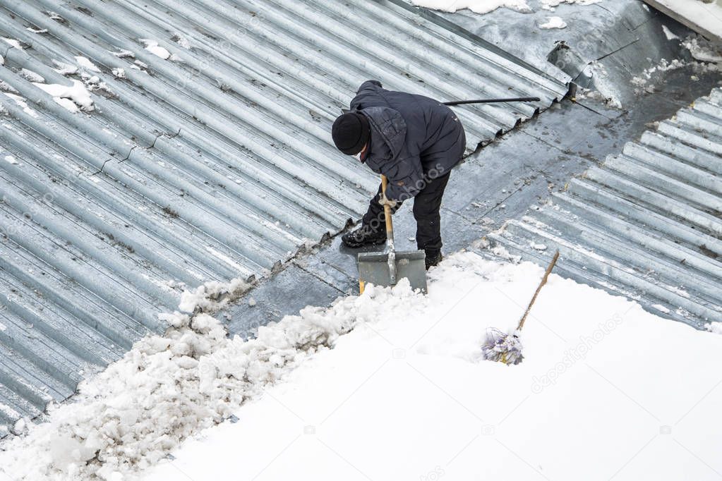 A man removes snow shovel top view, metal roof.
