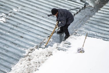 Bir adam kaldırır kar küreği üstten görünüm, metal çatı.