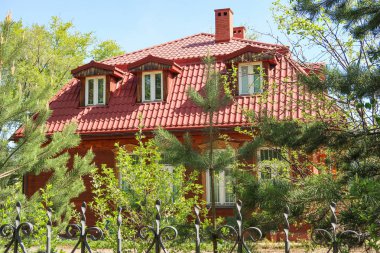 Bir metal çit arkasında Tuğla ev, bahar yeşil ağaçlar parkı.