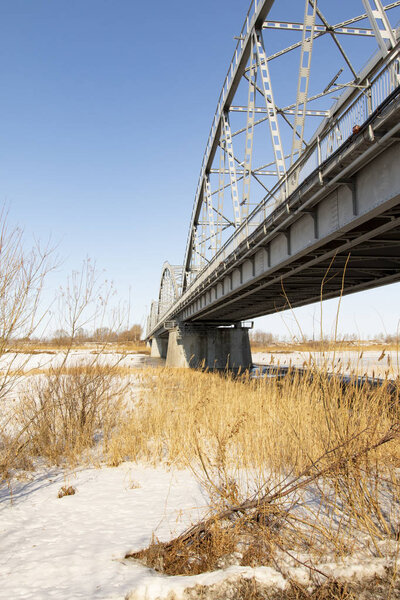 Metal arches of the bridge over the river. Winter, landscape.
