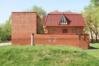 Bir metal çit arkasında Tuğla ev, bahar yeşil ağaçlar parkı.