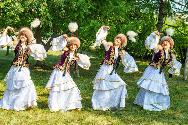 Petropavlovsk, Kazakhstan - August 17, 2019: Girls in national Kazakh clothes in hats. Summer day, green grass of a tree.