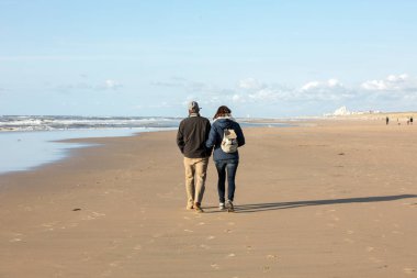 Katwijk, Hollanda - 23 Nisan 2017: Bir kadın ve bir adam Katwijk plaj boyunca güneşli bir günde yürüyor. Hollanda