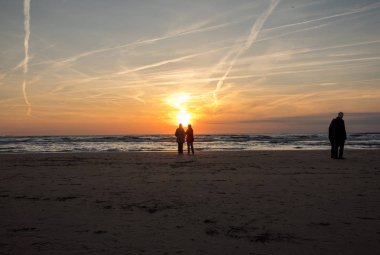 Katwijk, Hollanda - 23 Nisan 2017: İnsanlar günbatımında Katwijk plajda yürüyor. Hollanda