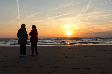 Katwijk, Hollanda - 23 Nisan 2017: İki kadın arıyor günbatımında Katwijk plajda. Hollanda