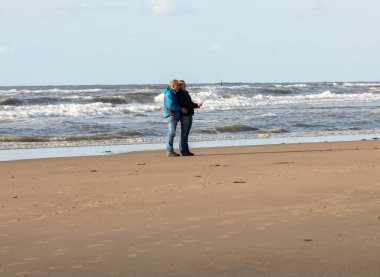 Katwijk, Hollanda - 23 Nisan 2017: Bir kadın ve bir adam Katwijk plaj boyunca güneşli bir günde yürüyor. Hollanda