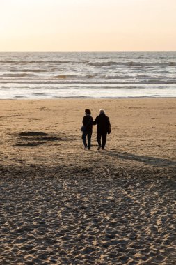 Katwijk, Hollanda - 23 Nisan 2017: Bir kadın ve bir adam Katwijk plaj boyunca güneşli bir günde yürüyor. Hollanda